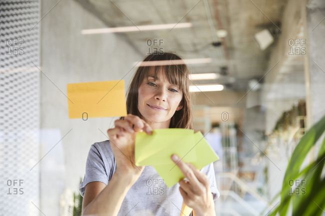 Mature woman sticking adhesive notes on glass material