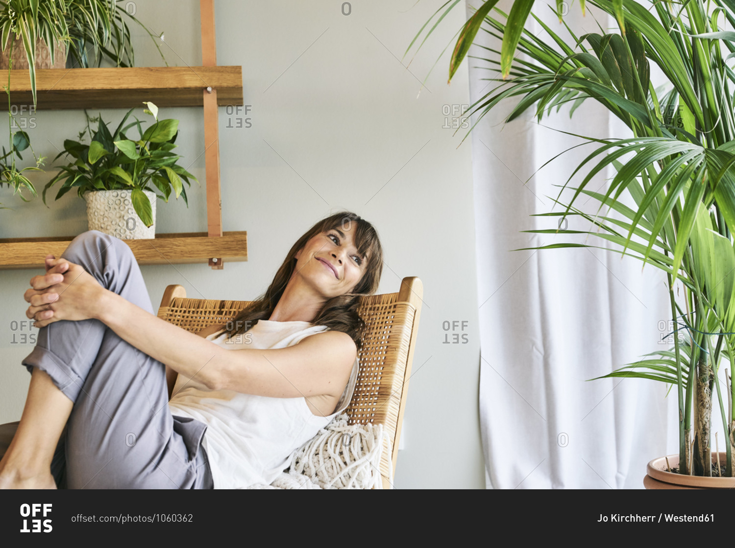 Smiling woman hugging knee while relaxing on chair at home