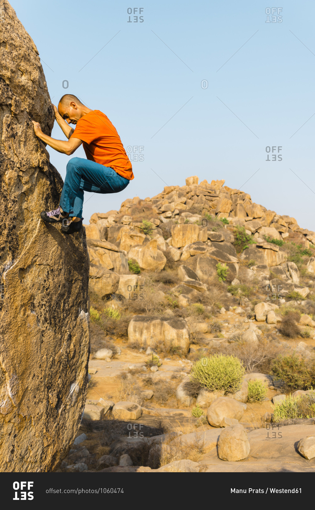 Male rock climber ascending rock wall with hill in background
