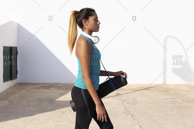 Young woman with exercise mat walking on sunny day