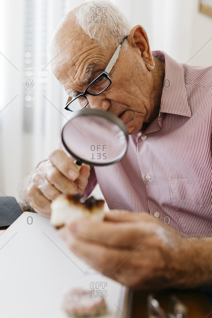 Elderly man examining minerals and fossils with magnifying glass while sitting at table