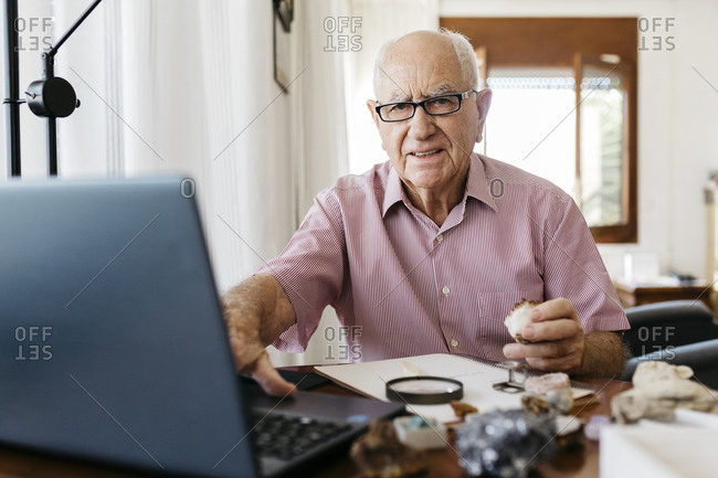 Retired senior man doing research on fossils and minerals while sitting with laptop at home