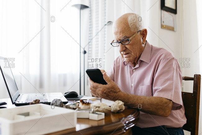 Senior man using smart phone while doing research on mineral and fossil at home