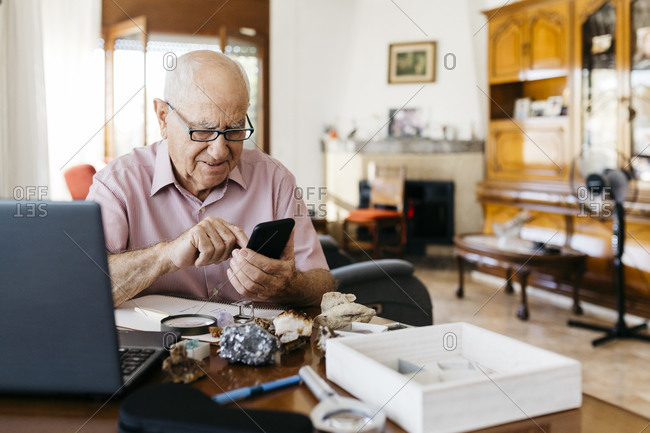 Elderly man using smart phone while doing research on mineral and fossil at home