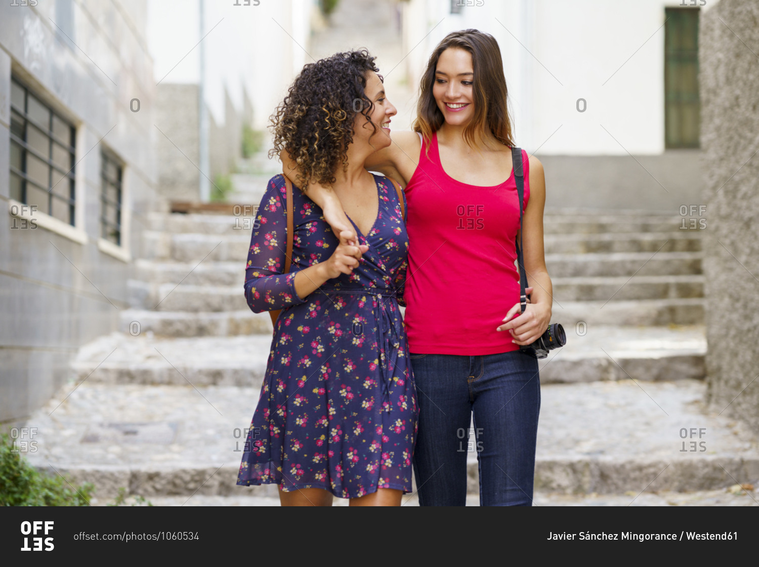 Couple with arm around shoulder smiling while walking on staircase in city