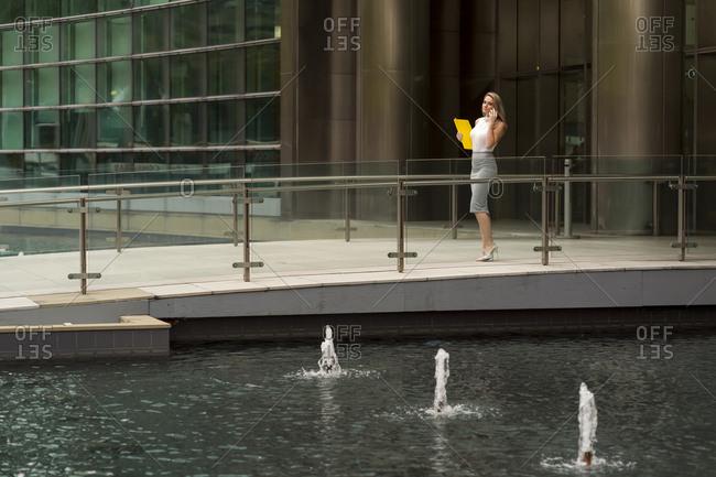 Businesswoman talking through smart phone while walking on footpath by fountain in city