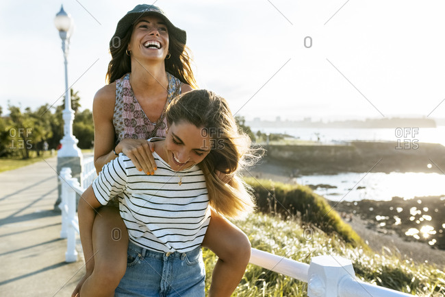 Carefree young woman piggybacking sister on footpath during sunny day