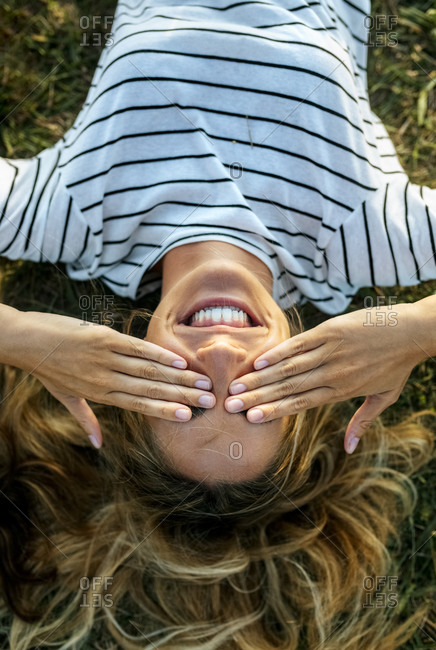 Happy young woman covering eyes with hands while relaxing on field