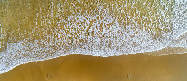 Aerial view of wave brushing sand of coastal beach