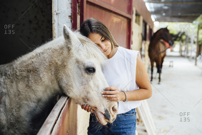 Young woman stroking pony standing in stable