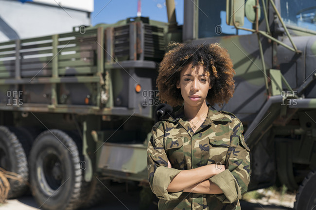Confident young female military soldier standing with arms crossed against truck at base on sunny day