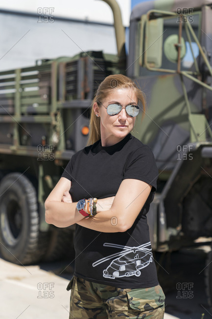Confident mature female army soldier standing with arms crossed while looking away against truck on sunny day