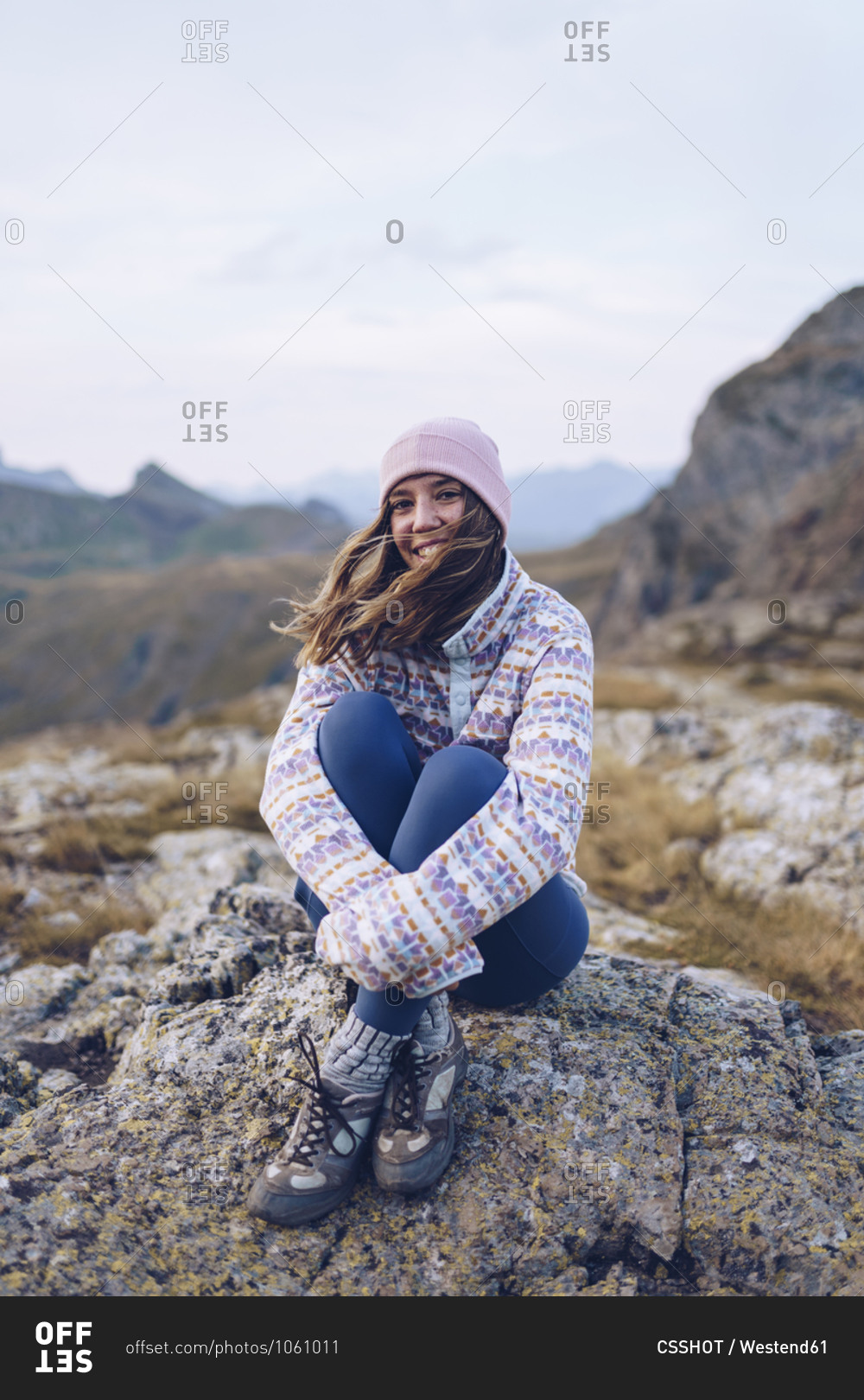 Smiling woman hugging knees while sitting on rock around Ibones of Anayet