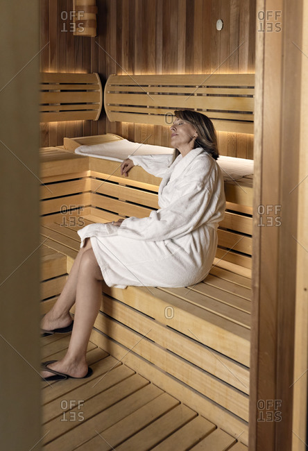 Thoughtful woman wearing bathrobe sitting on wooden sauna at health spa