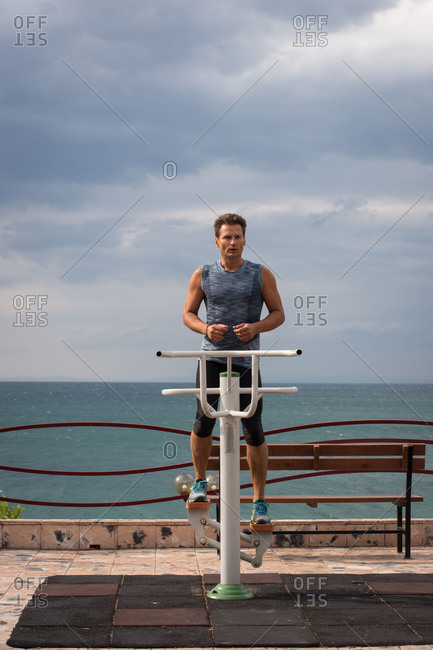 Adult man trains in the morning on sports equipment by the sea