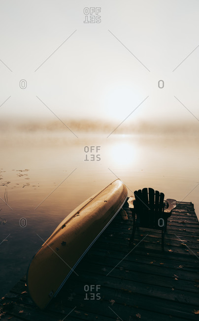 Empty dock with overturned canoe on a foggy morning on a calm lake.