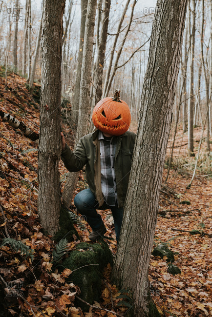 Man wearing scary carved pumpkin head in the woods for Halloween.