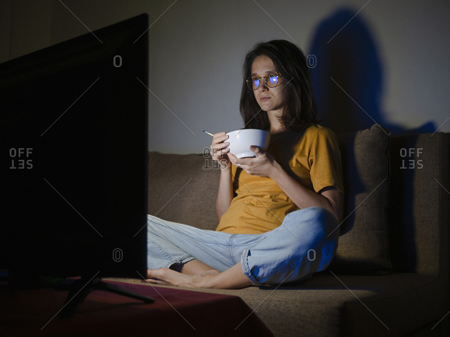 Young woman watching tv with food bowl in her room at evening time