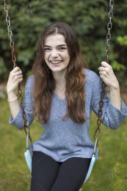 Pretty teen girl sitting on swing smiling with greenery in background
