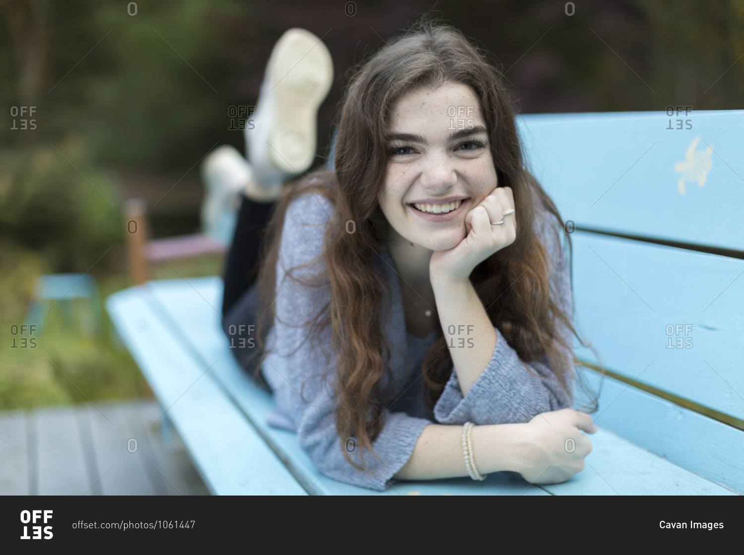 Pretty seventeen year-old girl lying on blue bench smiling stock photo ...