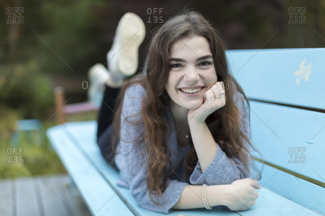 Pretty seventeen year-old girl lying on blue bench smiling