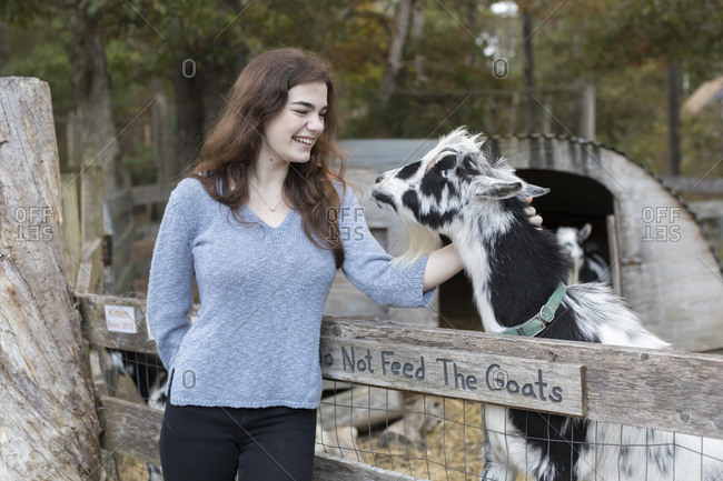 Pretty teenage girl smiling and petting goat in farm setting