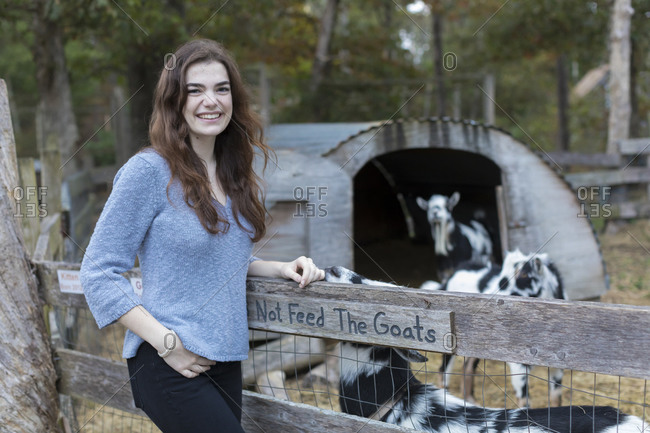 Portrait of pretty teenage girl smiling at goat pen in farm setting