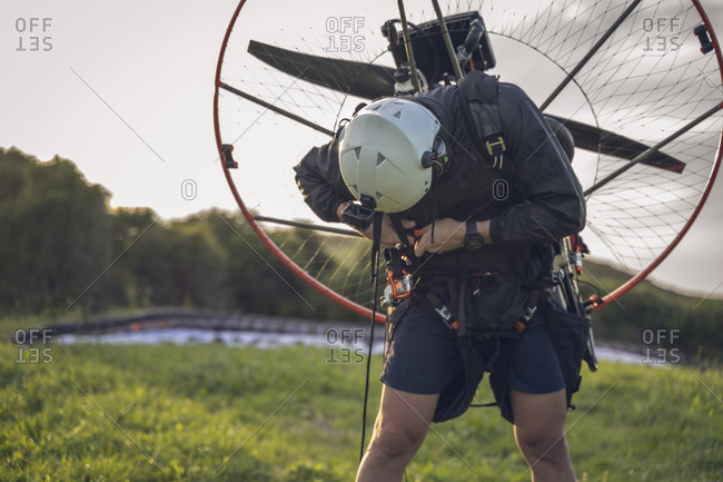 Young man, wearing a white helmet with an Action Cam on it, gets ready to fly with the Powered Paragliding ( Paramotor ) , and fastens his belt.