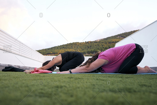 Two women practice yoga on the terrace of the house, child´s posture