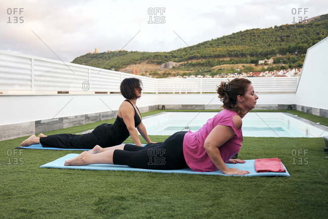 Two women practice yoga on the terrace of the house half cobra posture
