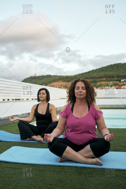 Two women practicing yoga on the terrace of the house, lotus posture