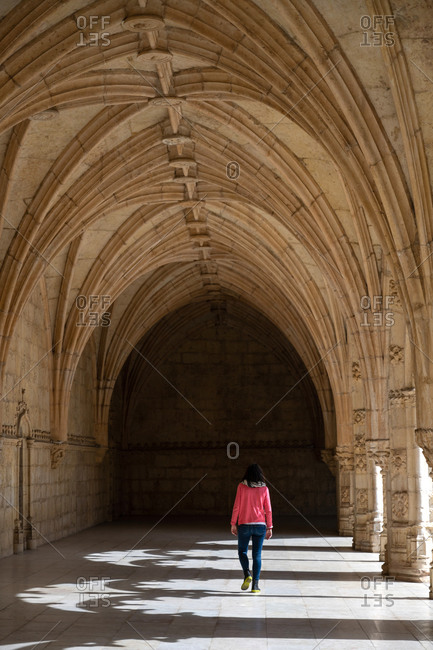 Rear view of traveler woman in pink jersey walking in ancient building