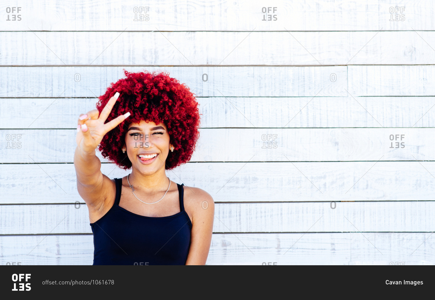 Portrait of woman with red afro showing victory symbol with fingers.
