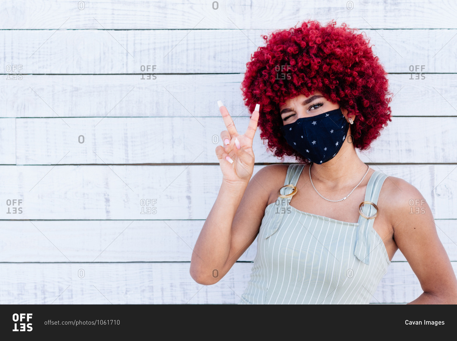 Latin women with mask and red hair showing a victory symbol.