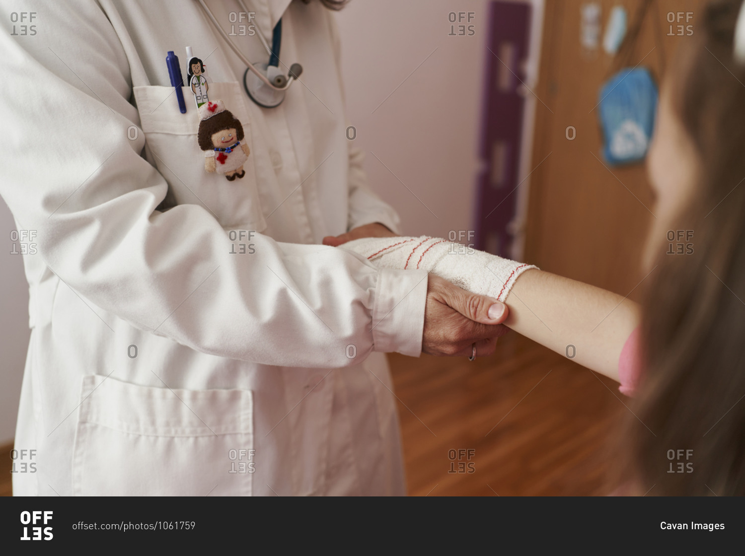 Side view of a female doctor bandaging the arm of a little girl in her room. Home doctor concept