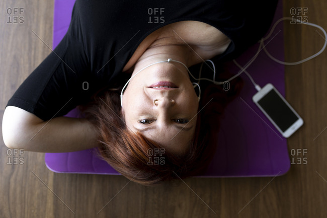Red hair woman laying on yoga mat listening to music