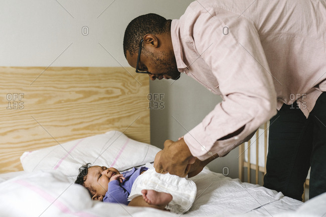Father changing babys diaper on bed