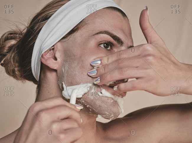 Shirtless androgynous young guy with manicure holding hand on waist and looking away while shaving face
