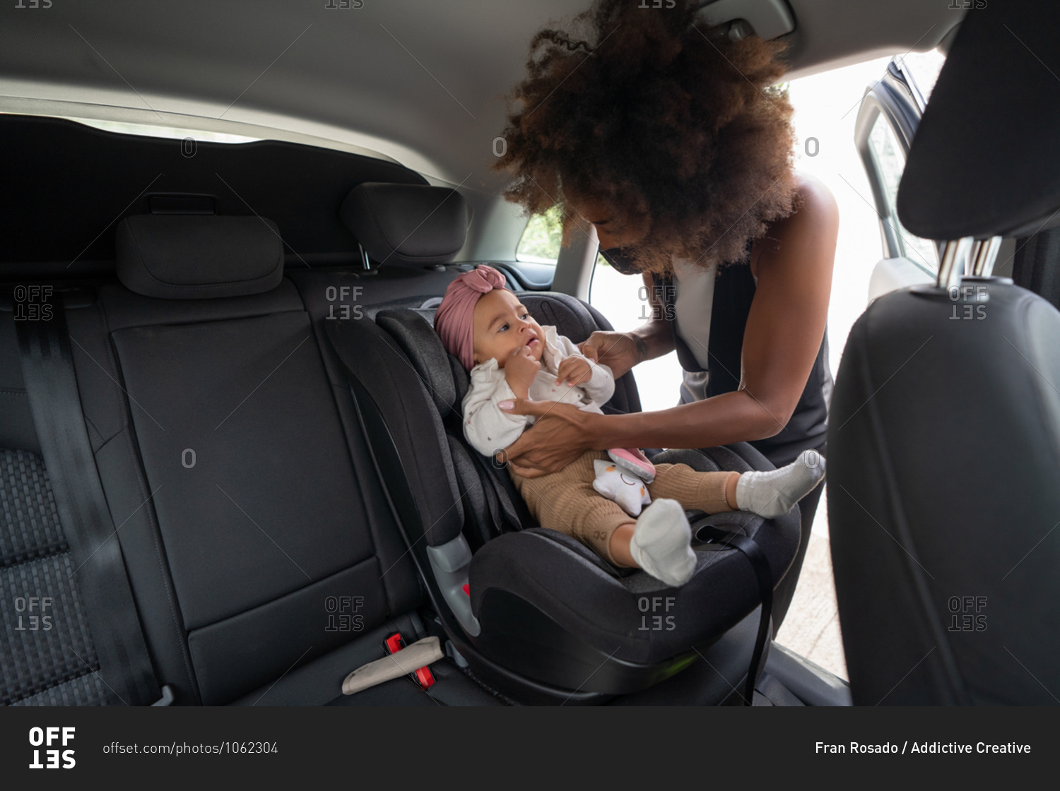 Caring African American mother tenderly putting cute toddler in modern baby car seat