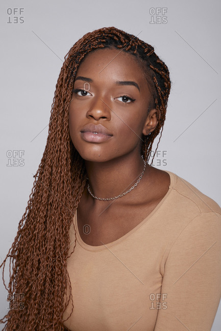 Relaxed African American female in casual outfit and with braids sitting on gray background in studio and tenderly looking at camera