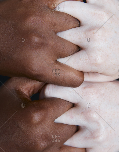 Top view of crop anonymous multiracial females tightly holding hands on black background in studio demonstrating concept of racial equality