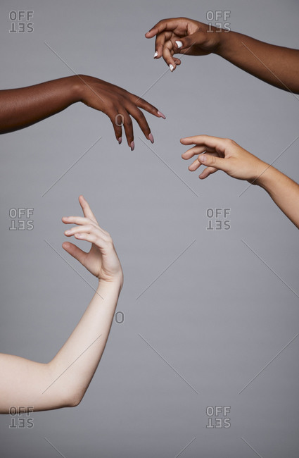 Crop faceless company of diverse females standing in studio with delicate raised arms on gray background