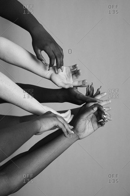 Black and white crop faceless company of diverse females standing in studio with delicate raised arms on gray background