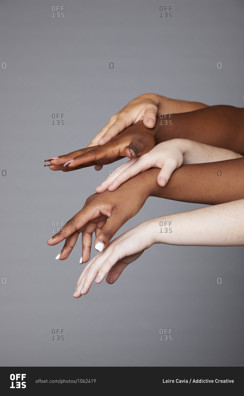 Group of unrecognizable crop multiracial females with different skin tone stacking hands delicately on gray background in studio demonstrating racial equality