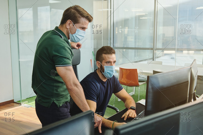 From above of male coworkers in medical masks together using program for software during coronavirus pandemic