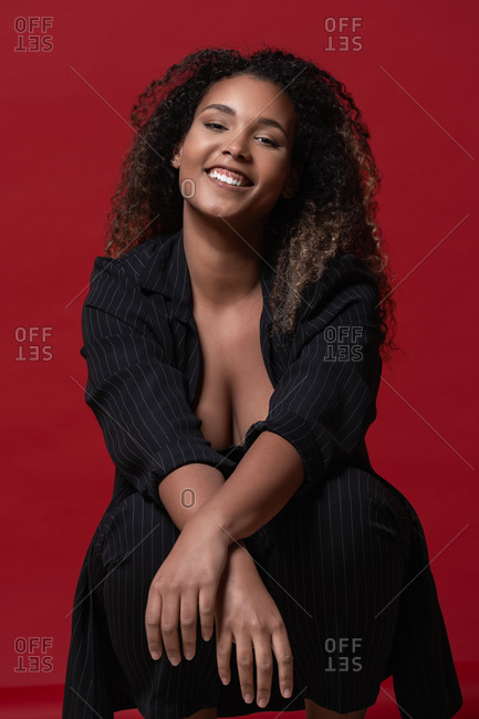 Beautiful confident happy young plus size black female model with long  curly hair wearing elegant black dress looking at camera against red  background stock photo - OFFSET