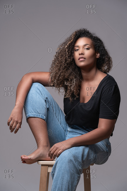 Beautiful confident young plus size black female model with long curly hair  wearing elegant black dress looking at camera against red background stock  photo - OFFSET