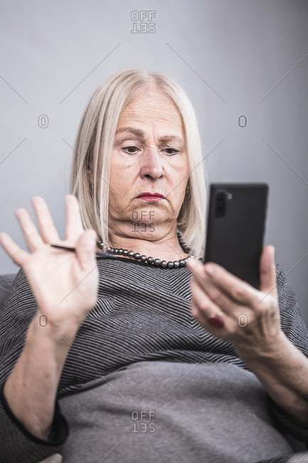 An elderly woman chatting on her cell phone with a stylus pen in hand