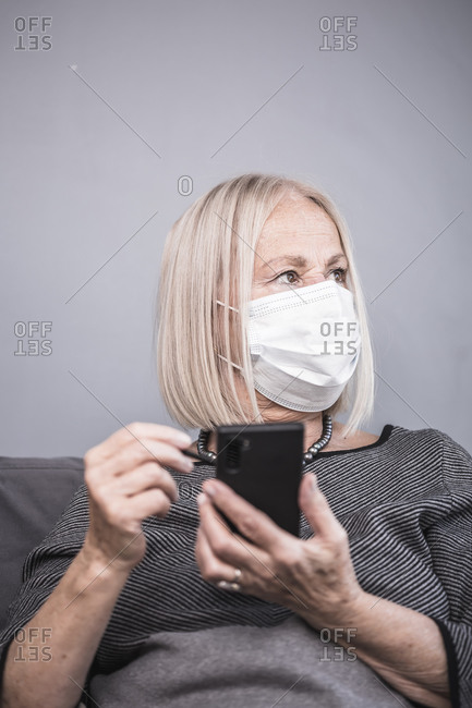 Senior woman using a cell phone with a stylus pen while wearing a facemask
