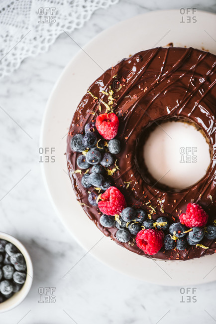 Top view of round chocolate cake topped with fresh fruit on a white marble counter